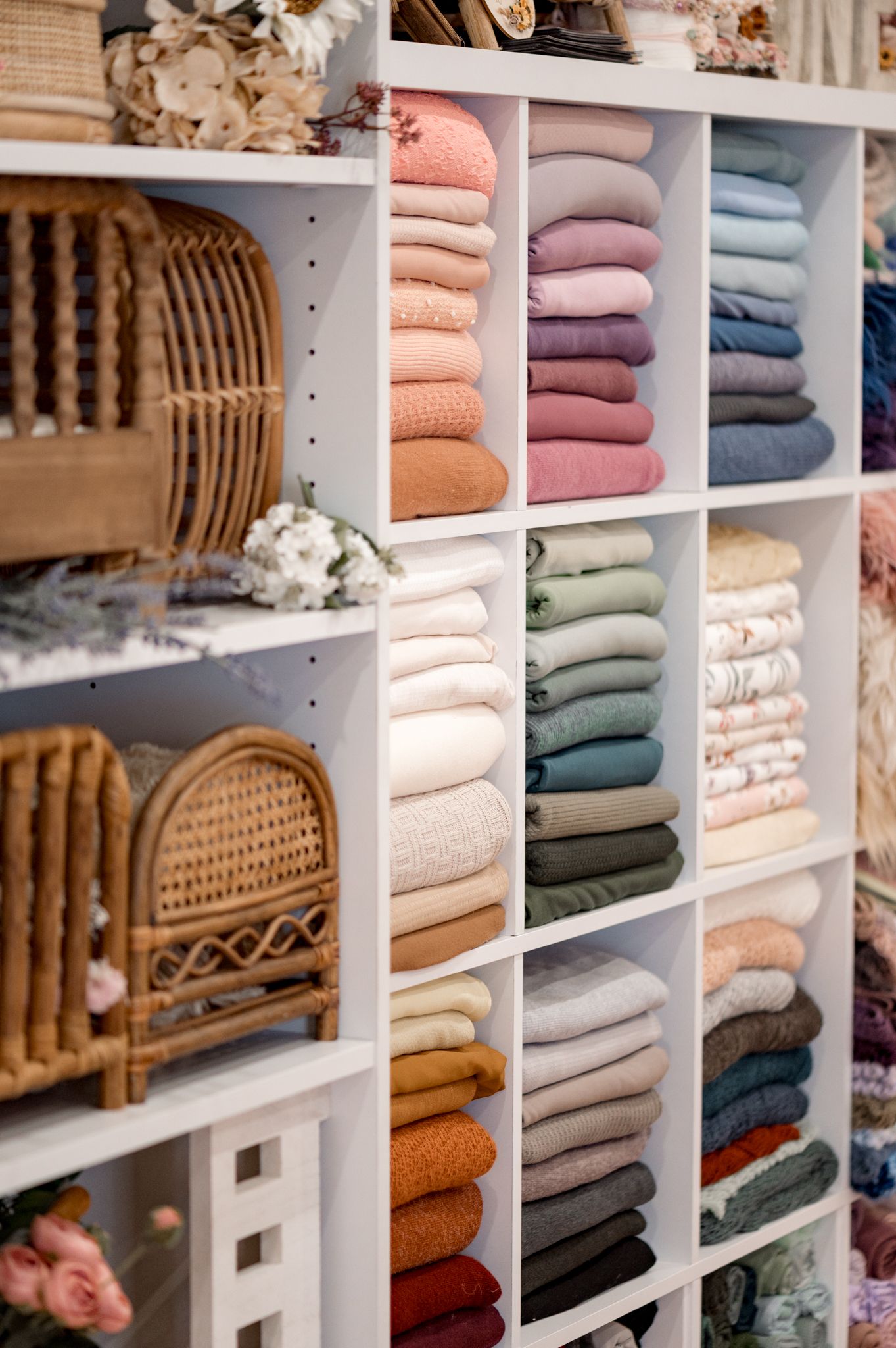White storage shelves filled with neatly folded sweaters in pastel and neutral colors alongside woven rattan decor items.