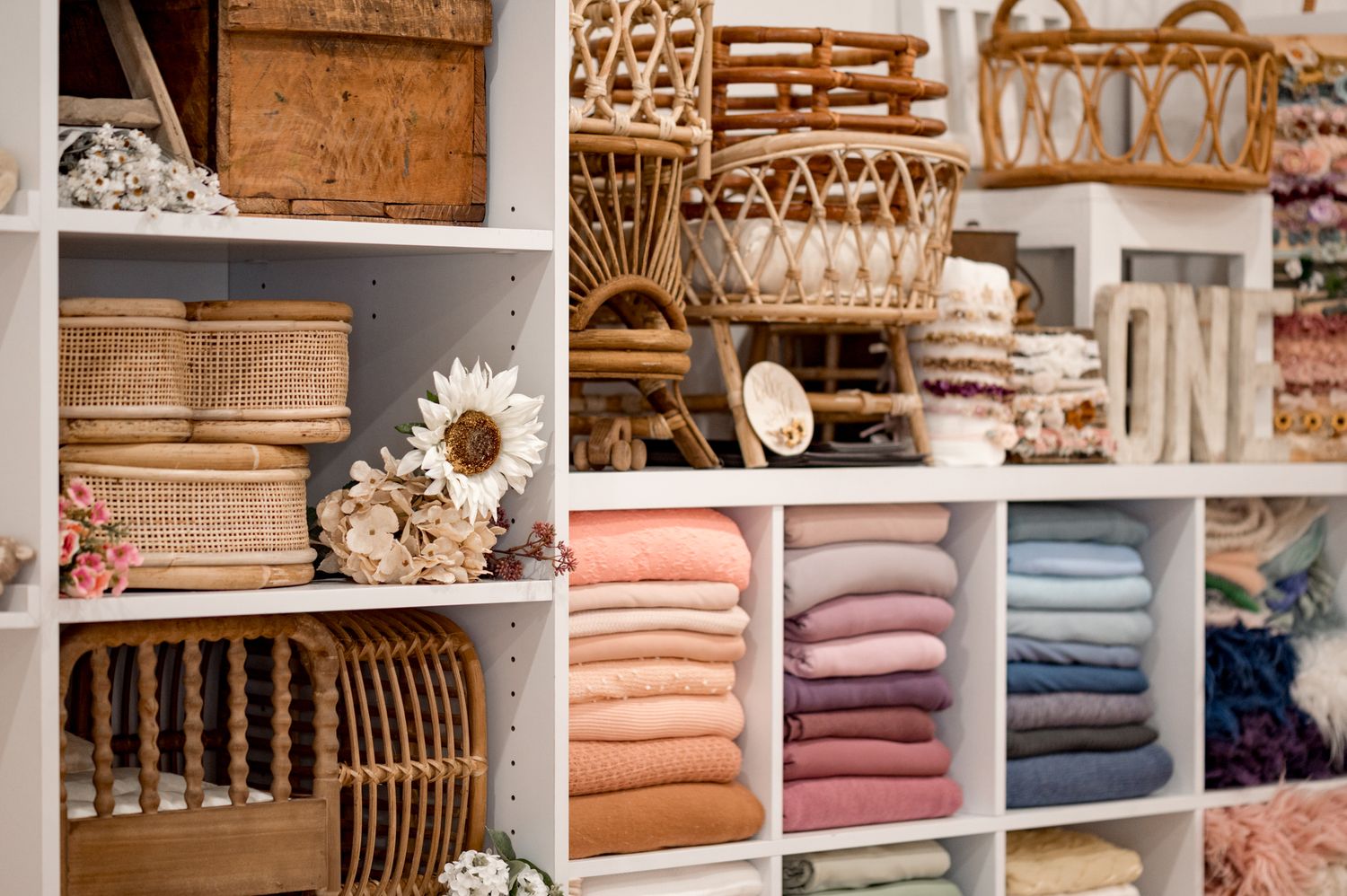 Retail display shelves showing neatly folded textiles, woven baskets, and decorative items in natural and pastel colors.
