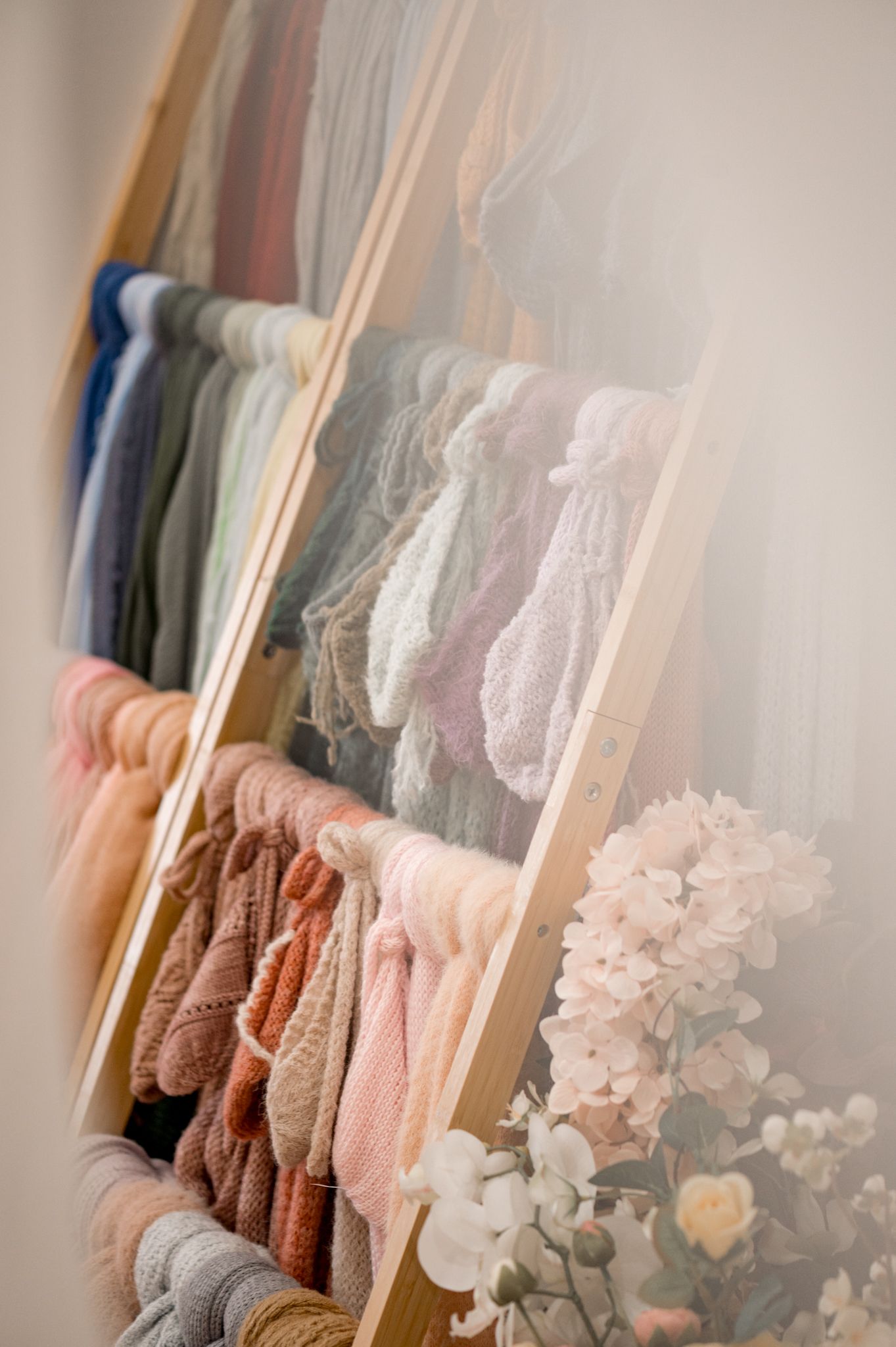 Clothing rack displaying soft pastel-colored sweaters and garments with delicate white flowers in the foreground.