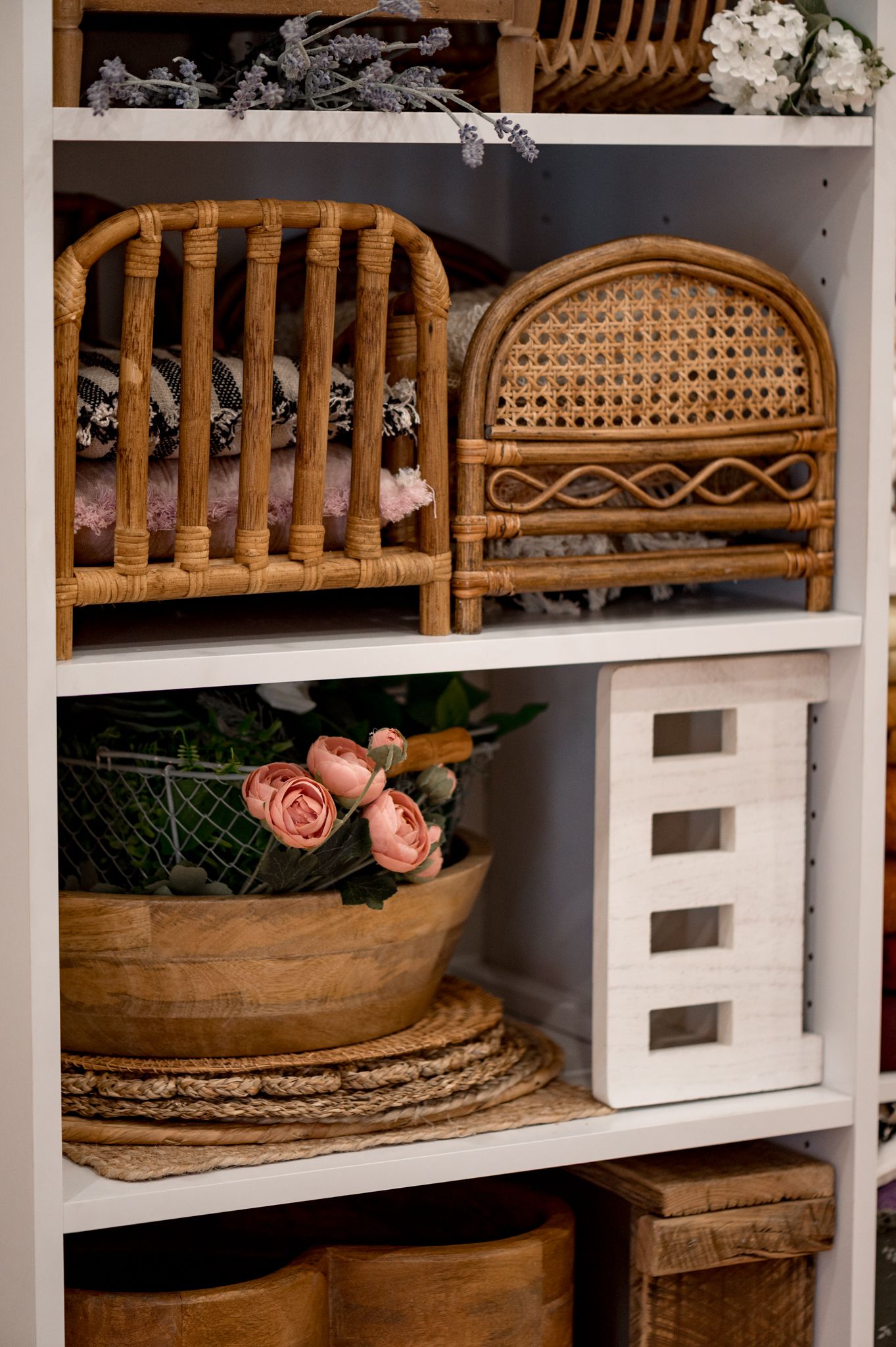 White shelving unit displaying vintage rattan headboards, artificial roses in wooden bowl, and rustic home decor elements.