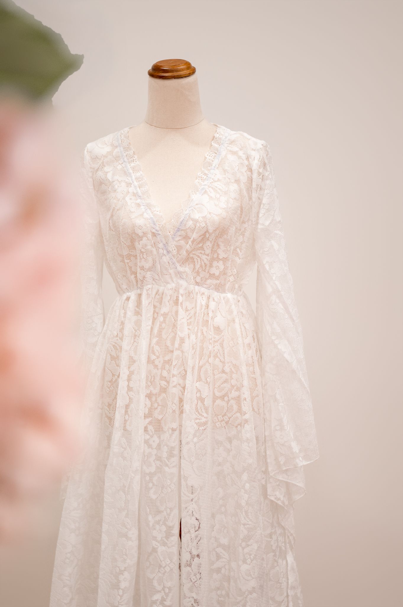 Beautiful white lace wedding robe with long bell sleeves and empire waist displayed on mannequin against soft blurred background.