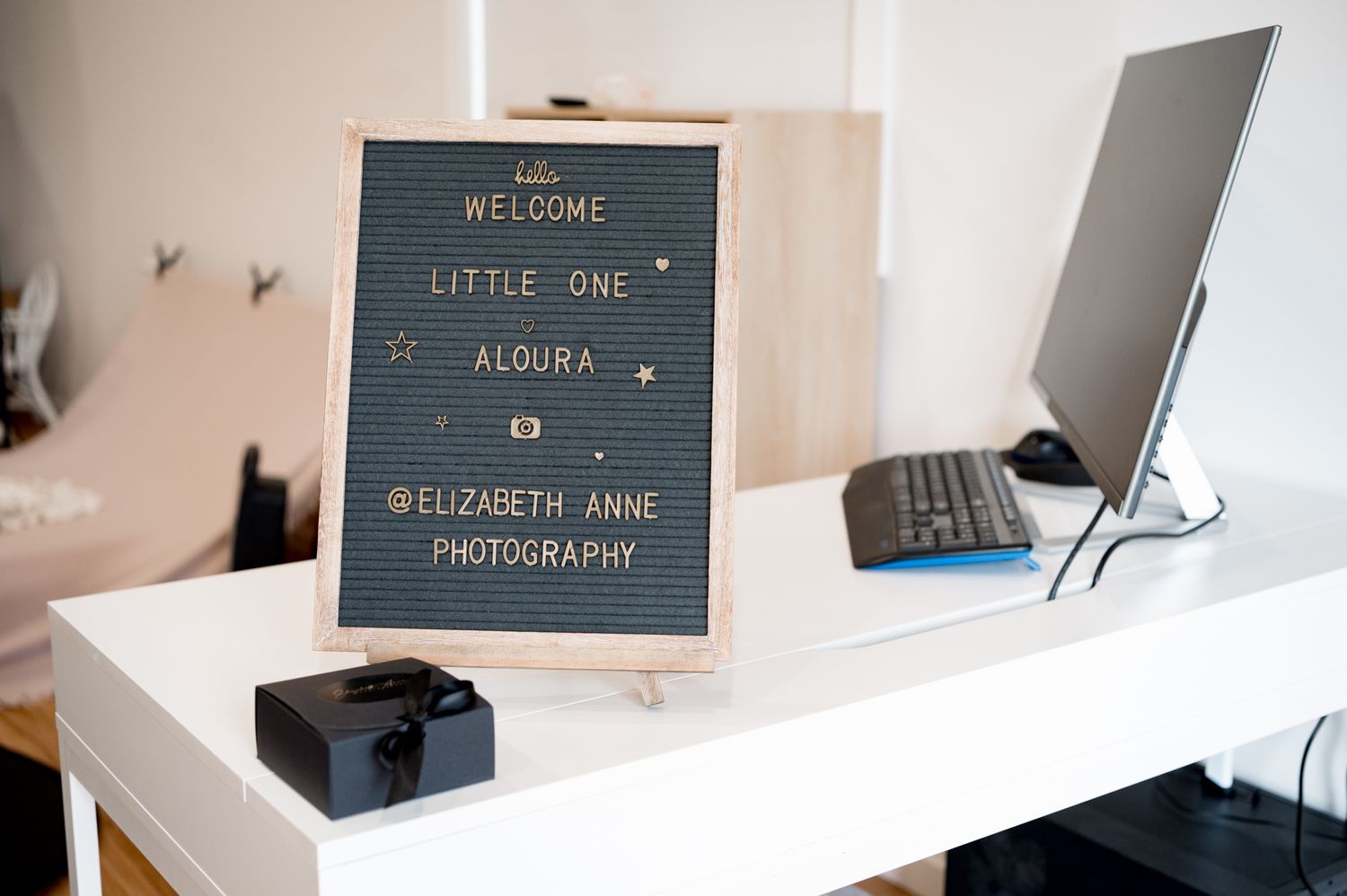 A black letterboard with welcome message sits on a white desk next to a laptop computer stand and monitor.