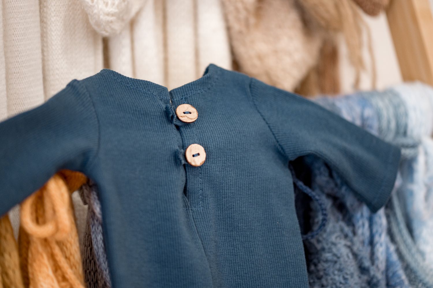 Close-up of vintage blue cotton baby dress with decorative white buttons hanging on display with other garments.