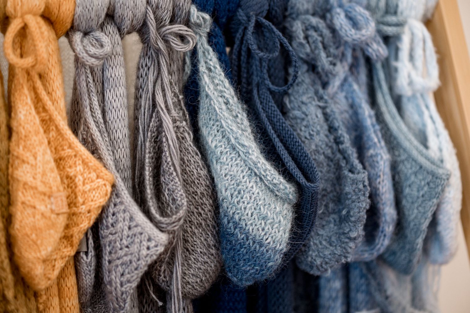 Close up view of cozy knit sweaters in various shades of blue, gray and orange hanging on a clothing rack.