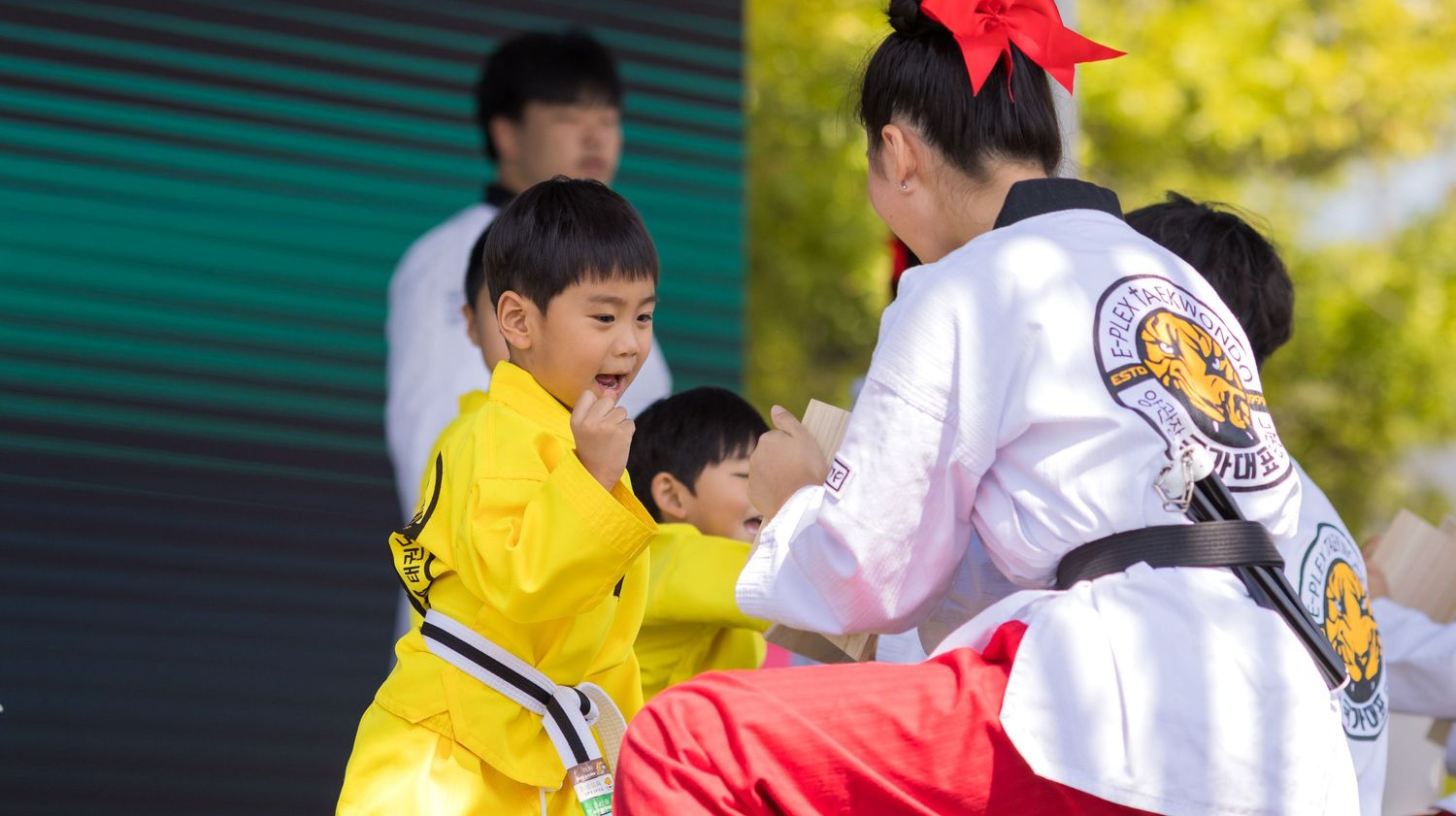 Two students practicing martial arts sparring in yellow and white uniforms with a red bow accent during training.