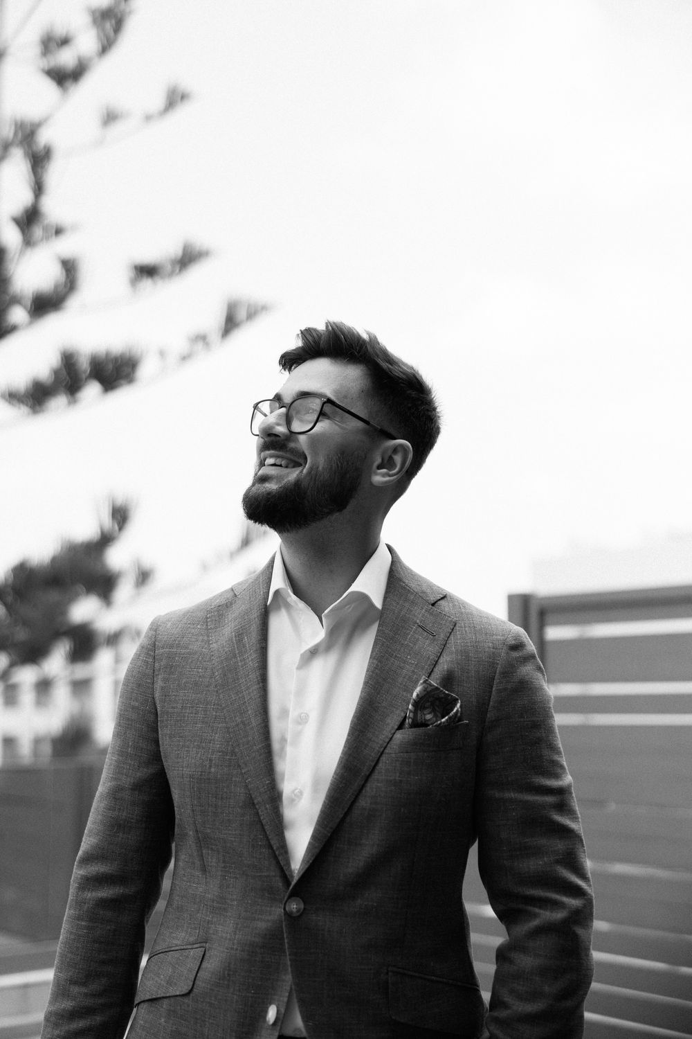Stylish man in grey suit and glasses smiling outdoors in black and white portrait. Wedding Agreco Farms, Crete