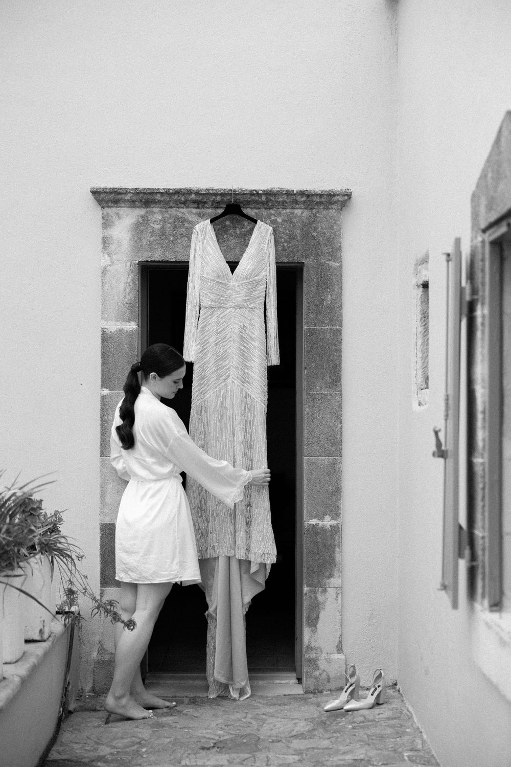 Person in robe reaching for hanging wedding dress in stone doorway. Wedding Agreco Farms, Crete