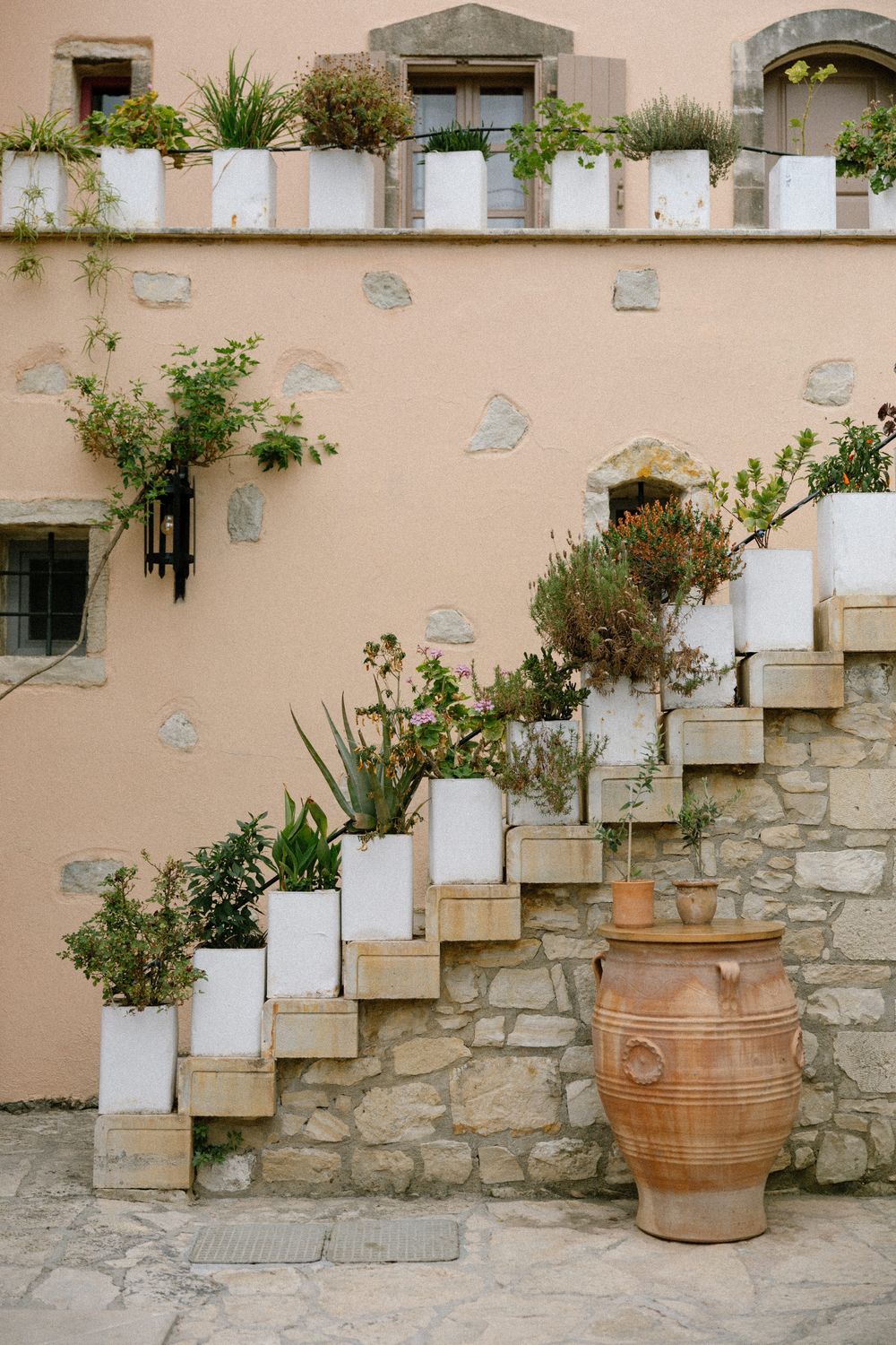 White planters arranged on stone steps against a peach-colored wall with a terra cotta pot at the base. Wedding Agreco Farms, Crete