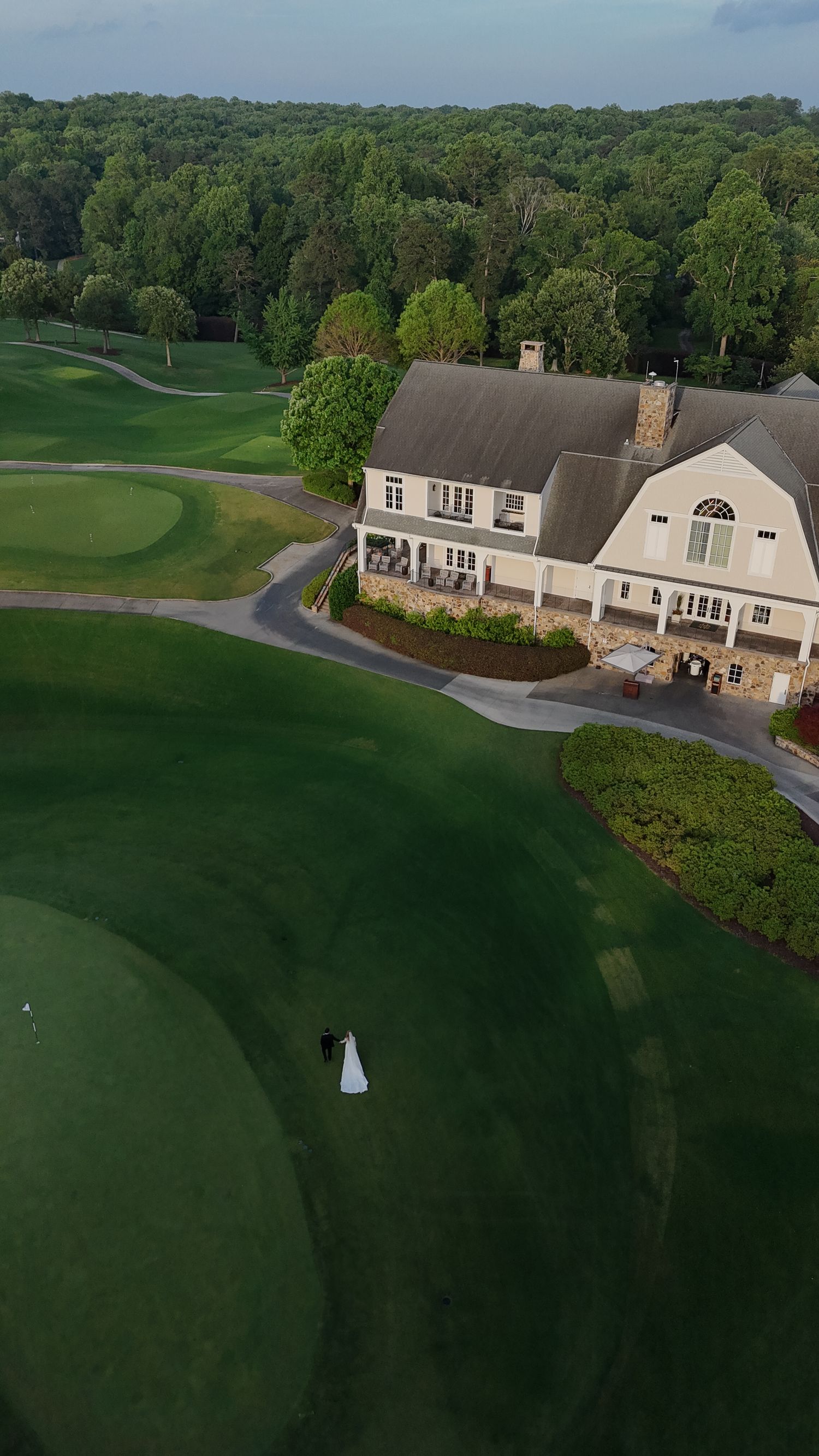 Aerial view of a luxury Martha's Vineyard golf clubhouse with beige exterior nestled among rolling green fairways and mature trees.