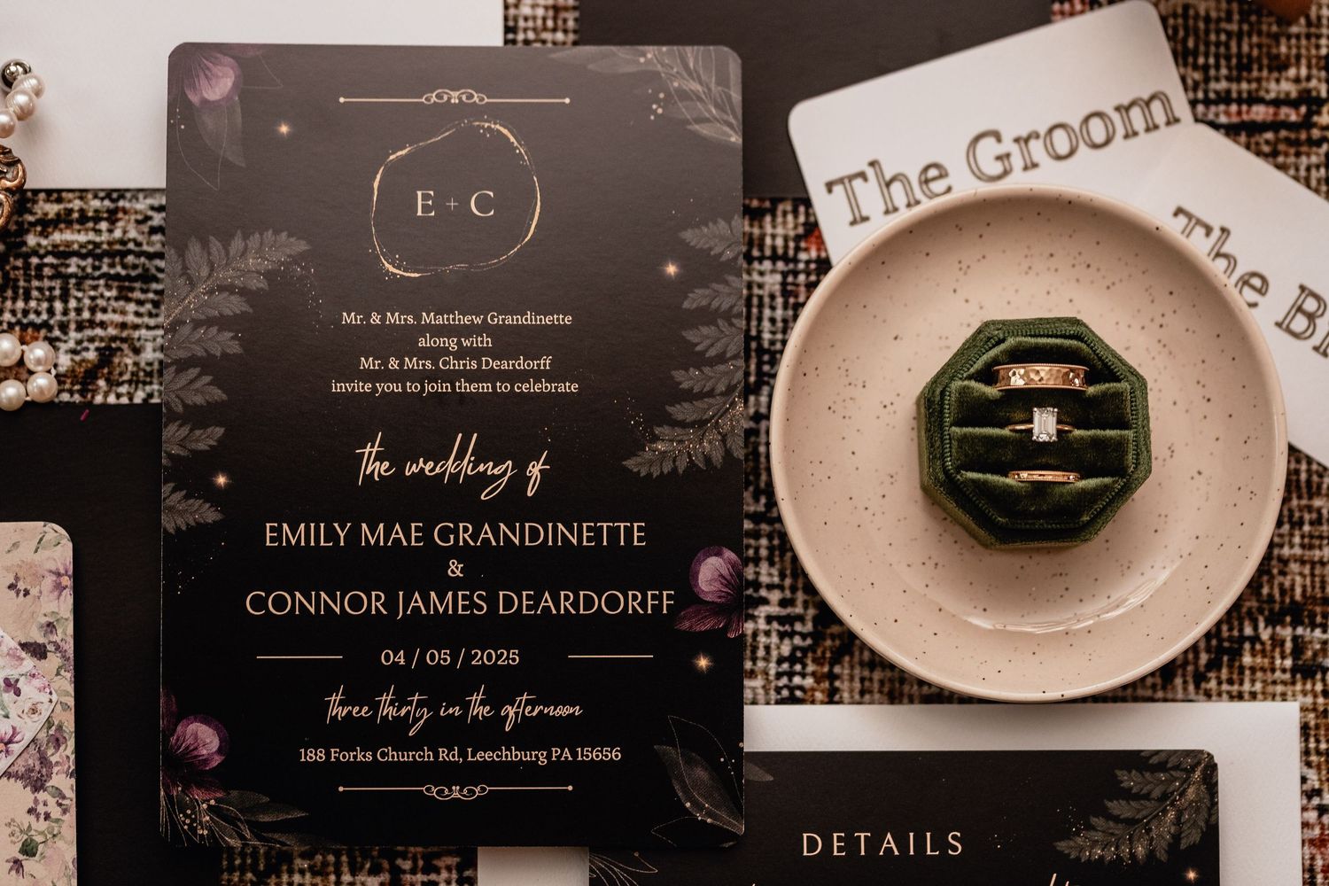 Flat lay wedding detail photo featuring elegant black and gold invitation suite, green velvet ring box with wedding bands