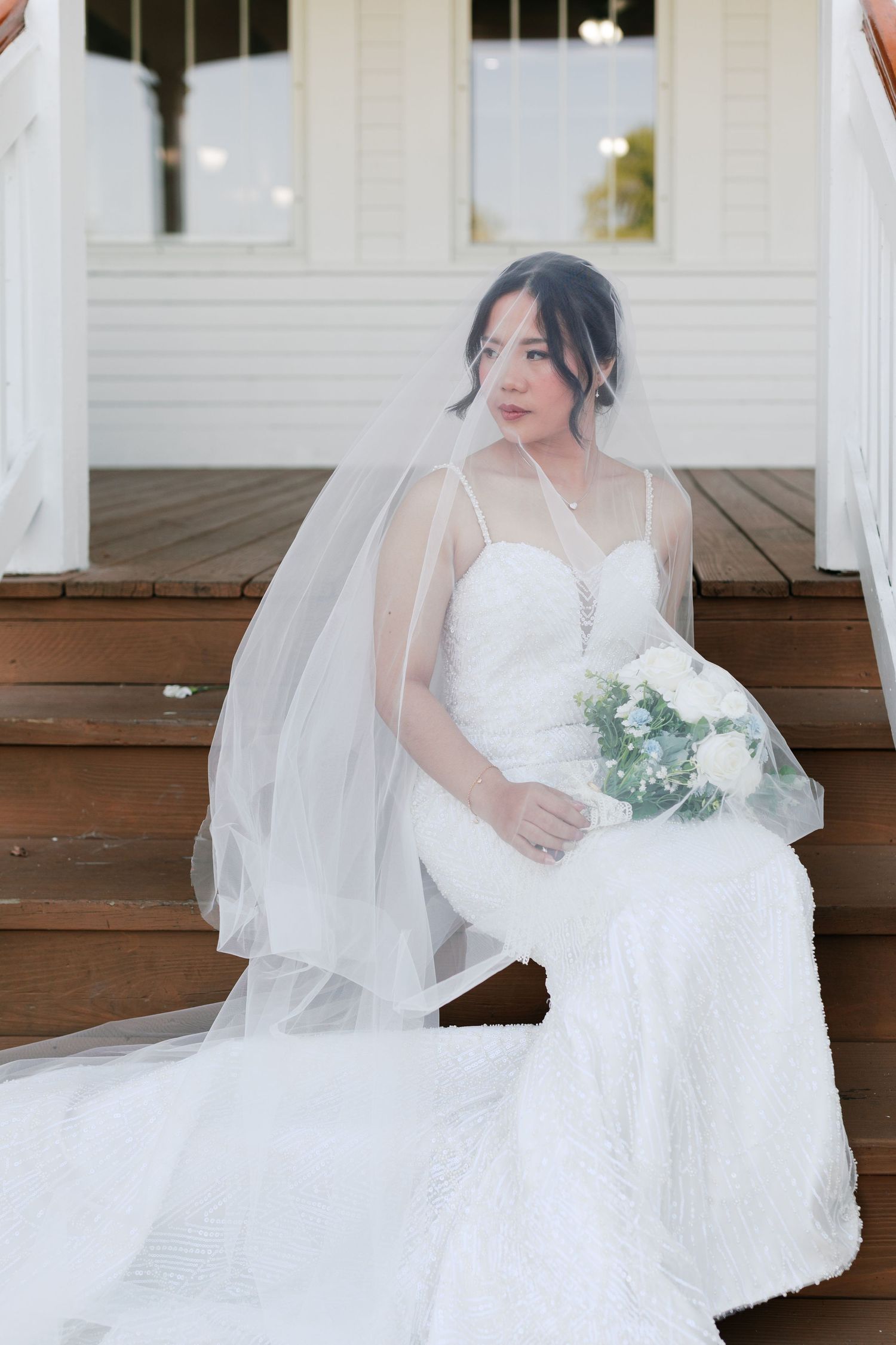 Elegant bridal portrait on wooden steps featuring a flowing white dress and delicate veil.