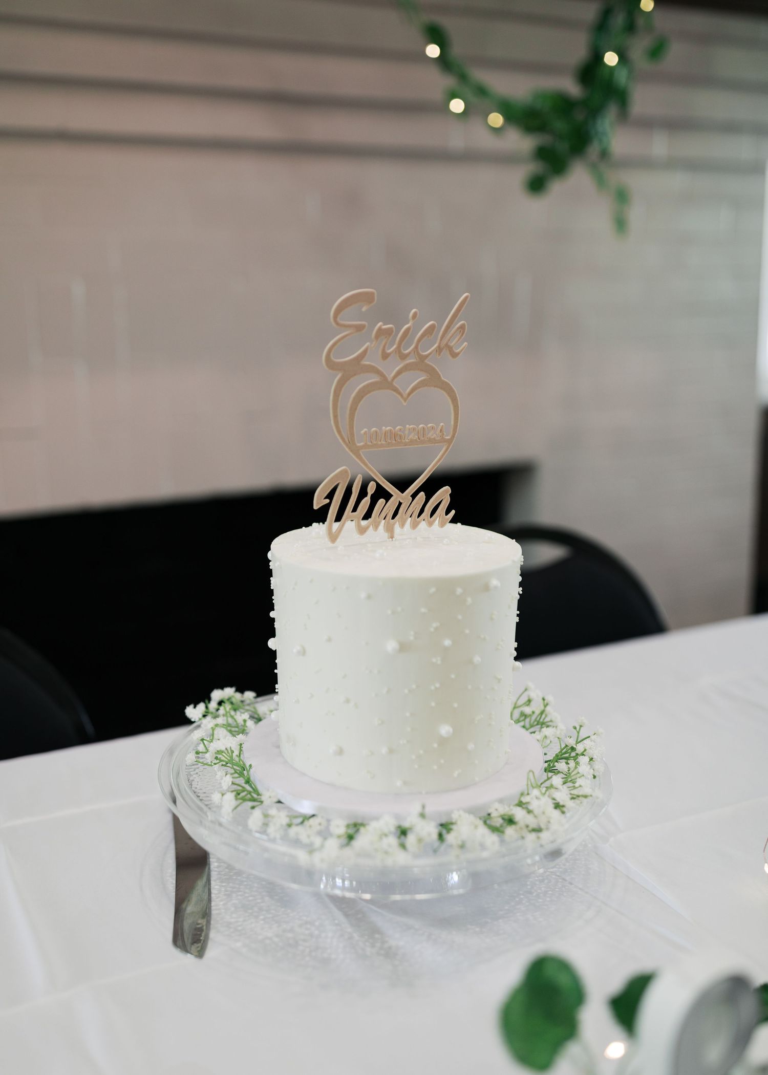 A white wedding cake decorated with small dots and a golden cake topper.