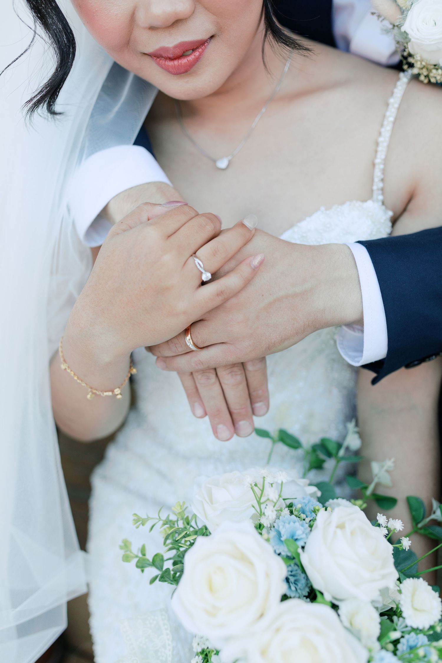Close-up of wedding rings and a white rose bouquet with delicate jewelry details.