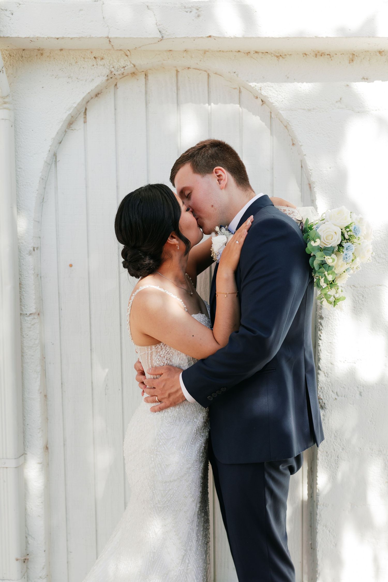 A tender moment between newlyweds in front of a white arched doorway.