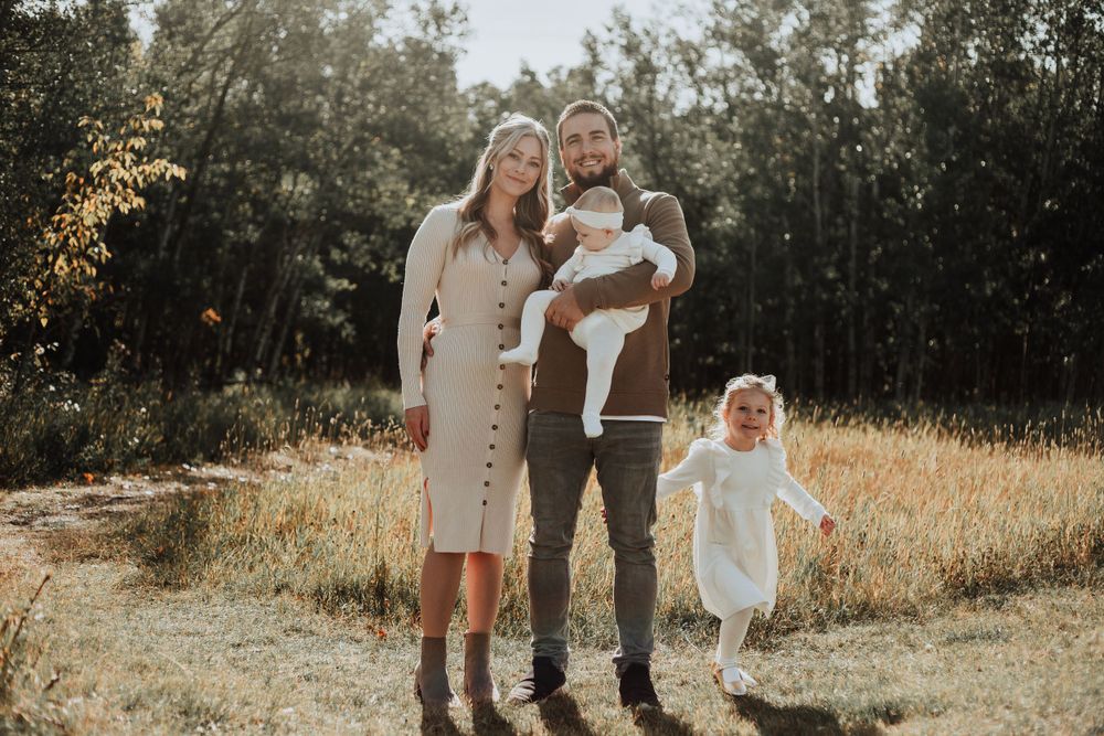 Family portrait in a sunlit field with golden grass and forest backdrop.