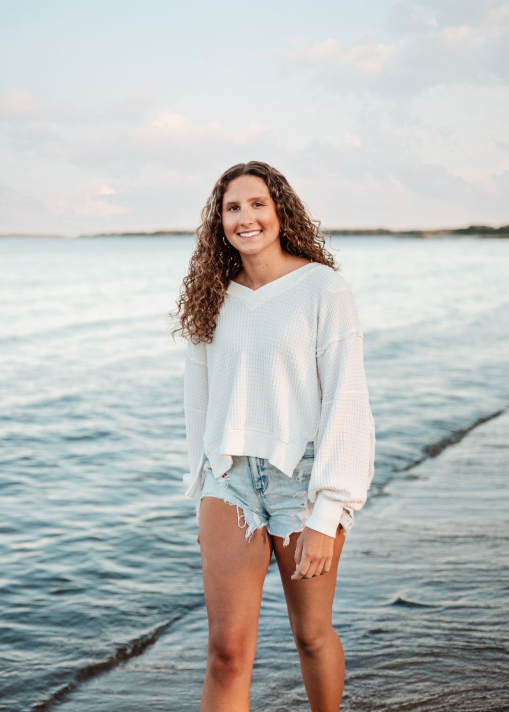 Beachwear portrait on ahore wearing white sweater and denim shorts at sunset.
