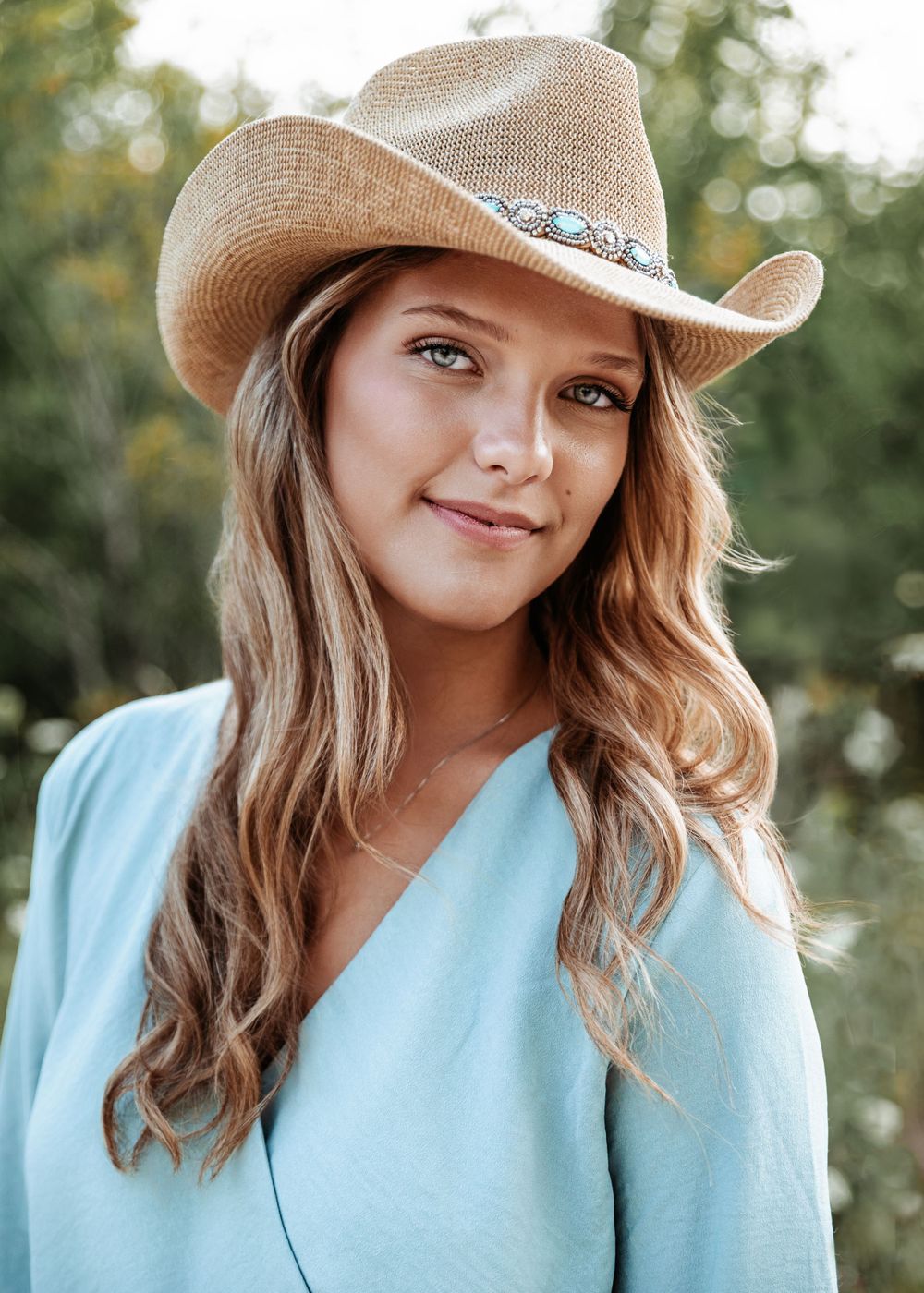 Outdoor portrait in turquoise top and cowboy hat with natural lighting.