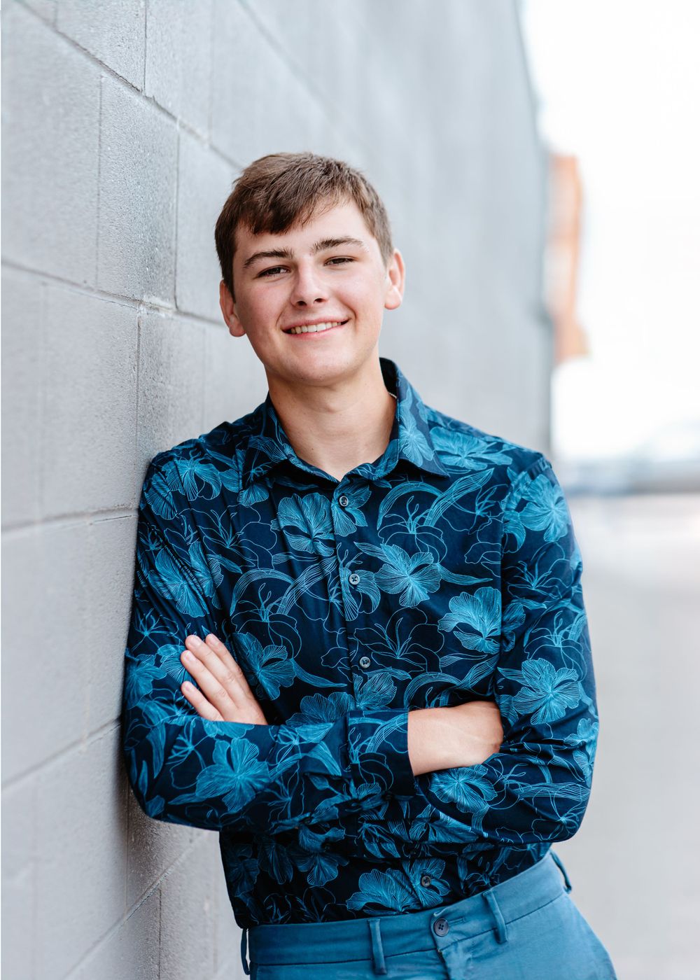 Portrait against gray wall wearing blue floral print shirt with crossed arms.