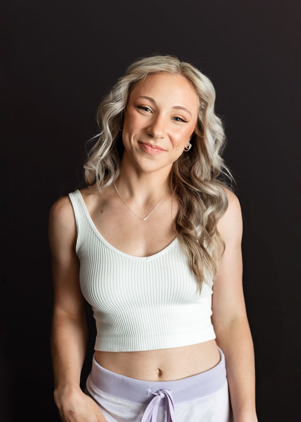 Studio portrait against black background featuring woman in white tank top with wavy blonde hair.