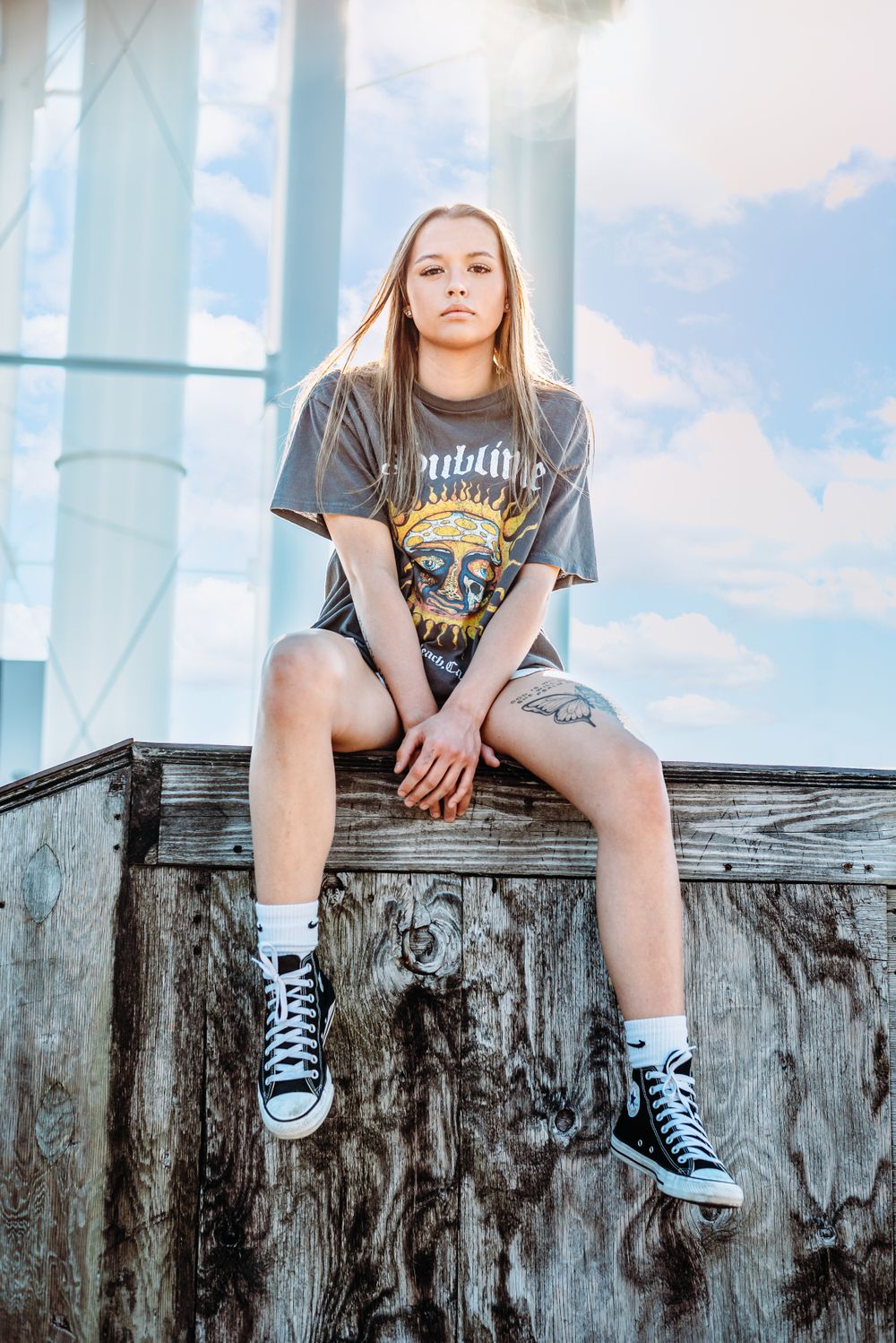 Edgy urban portrait of a person in vintage band tee and converse sneakers sitting on concrete wall.