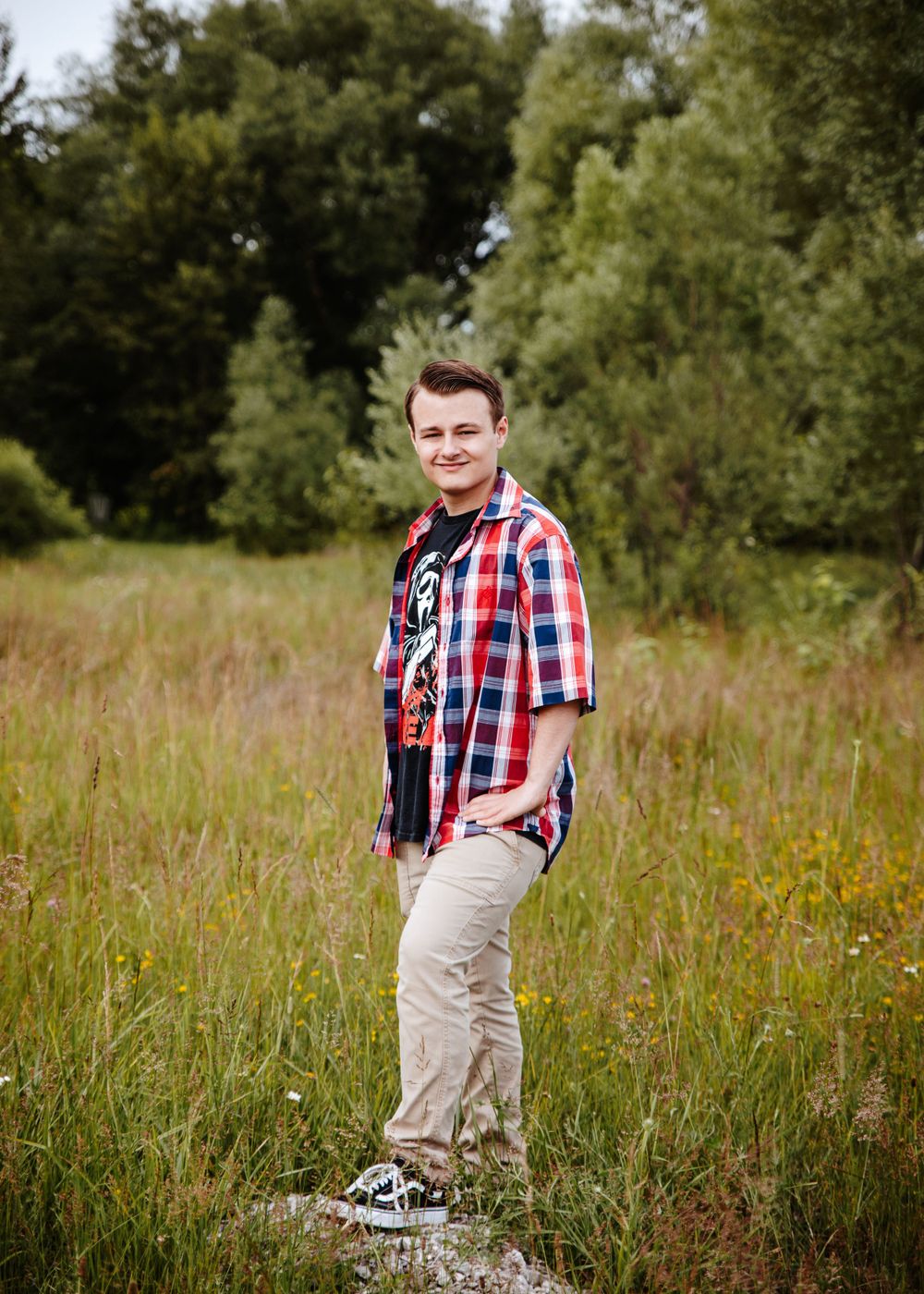 Casual outdoor portrait in plaid shirt standing in wild grass field.