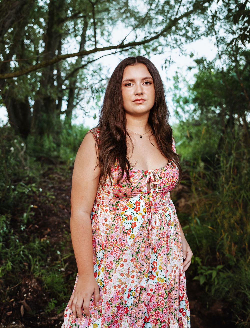 Natural outdoor portrait in floral summer dress among trees and greenery.