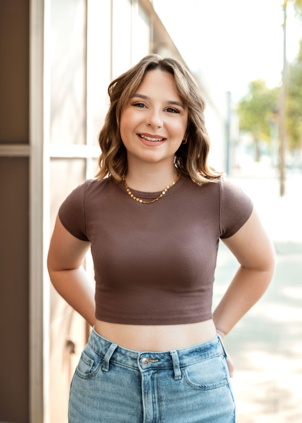 Young person in a brown crop top and jeans poses confidently indoors.