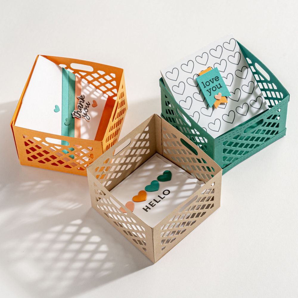 Three decorative paper gift boxes with geometric cutout patterns in orange, white, and teal colors.