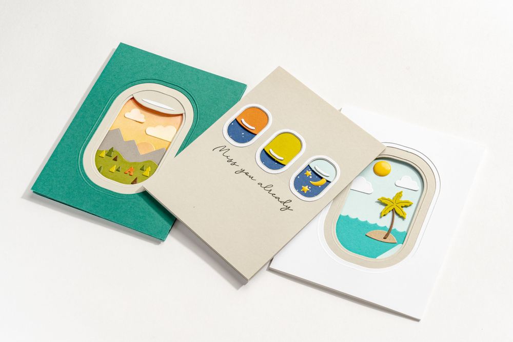 Three colorful greeting cards featuring tropical designs with windows and palm trees laid out on a white surface.