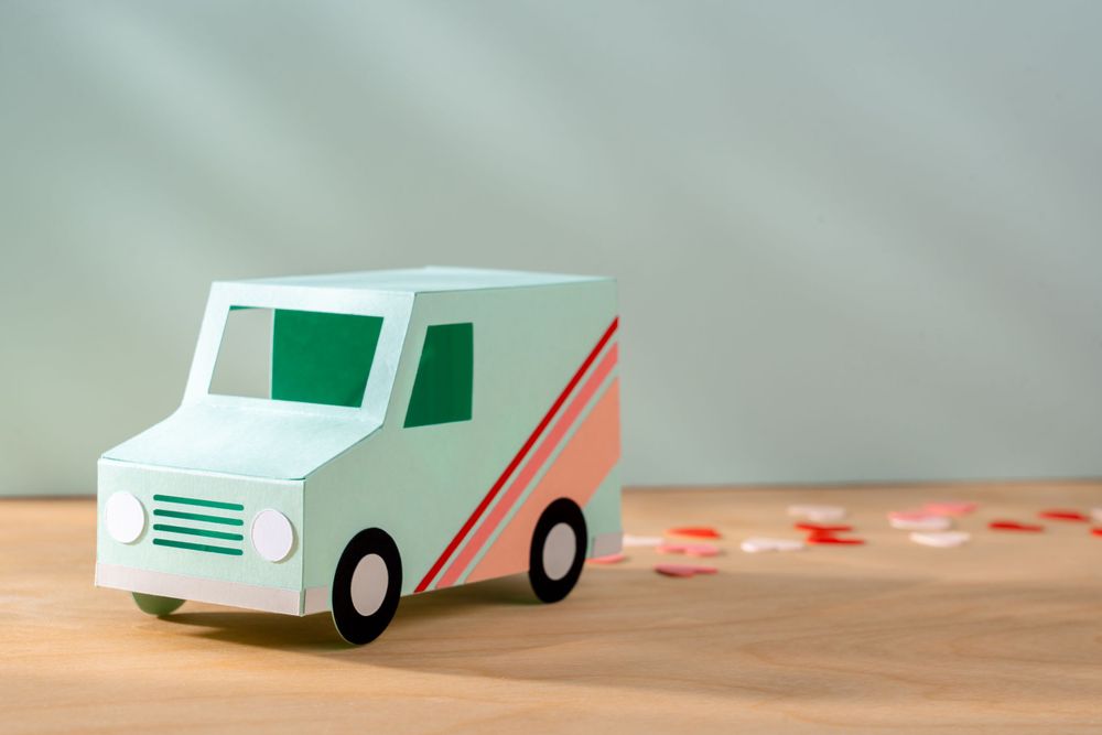 Miniature white and coral delivery van toy on wooden surface with decorative elements.