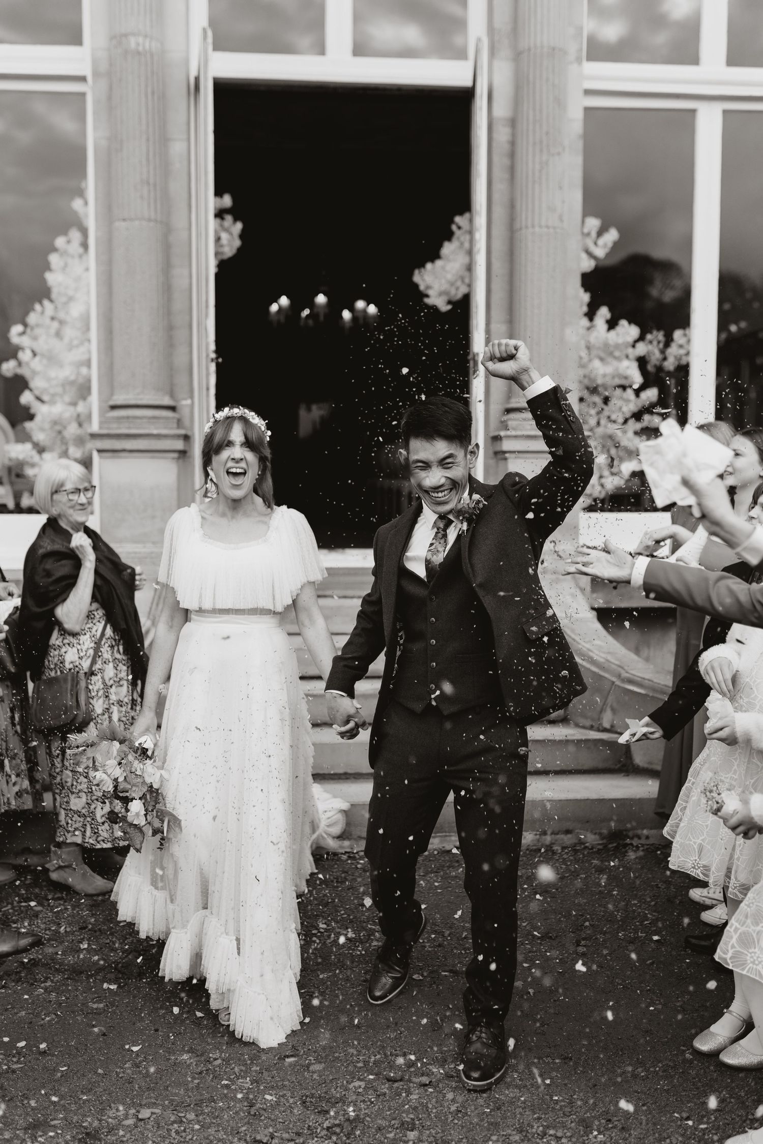 A couple exits a church building as wedding guests shower them with confetti in a classic black and white photograph at Berwick House.