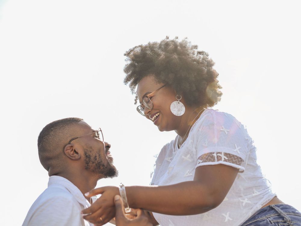 Couple shares romantic moment on beach rocks during engagement photography session.
