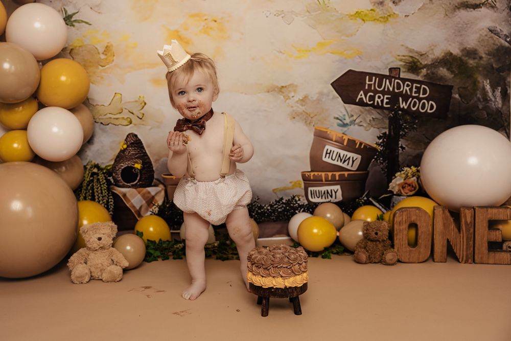 A rustic woodland-themed birthday setup with balloons, pumpkins, signage and a small cake on a stand.