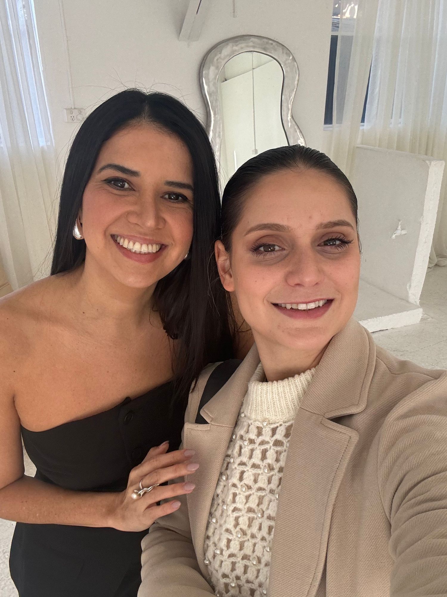 Two colleagues in business attire taking a friendly selfie in an office setting.
