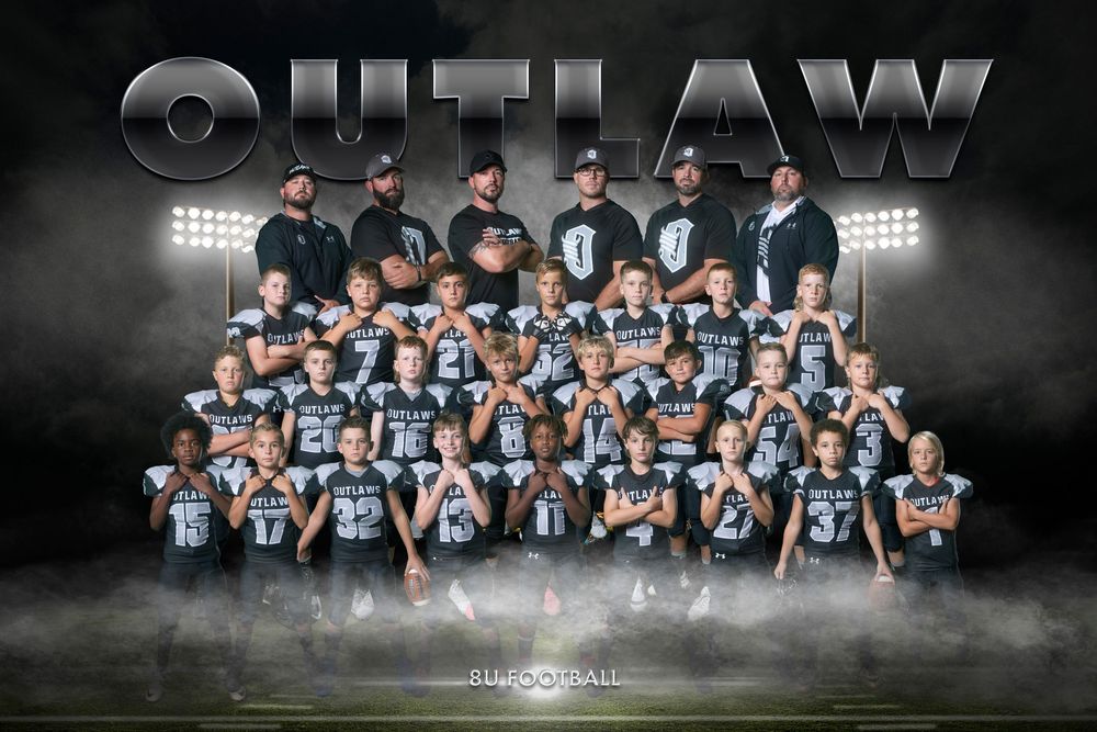 Youth football team photo with players and coaches arranged in rows against dramatic dark background with stadium lights.