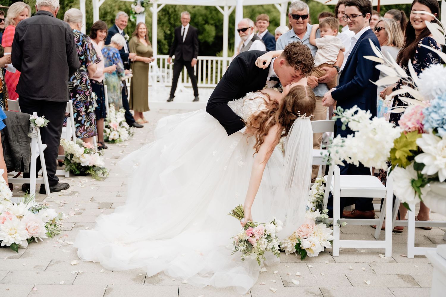 Wedding couple shares romantic dip kiss during outdoor ceremony.