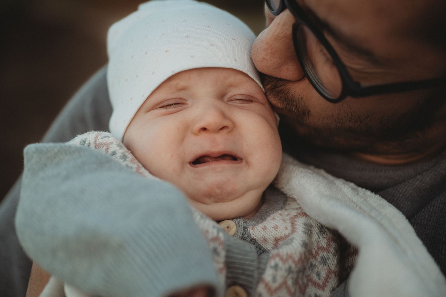 A close-up capture of a laughing baby in a white hat being held lovingly.