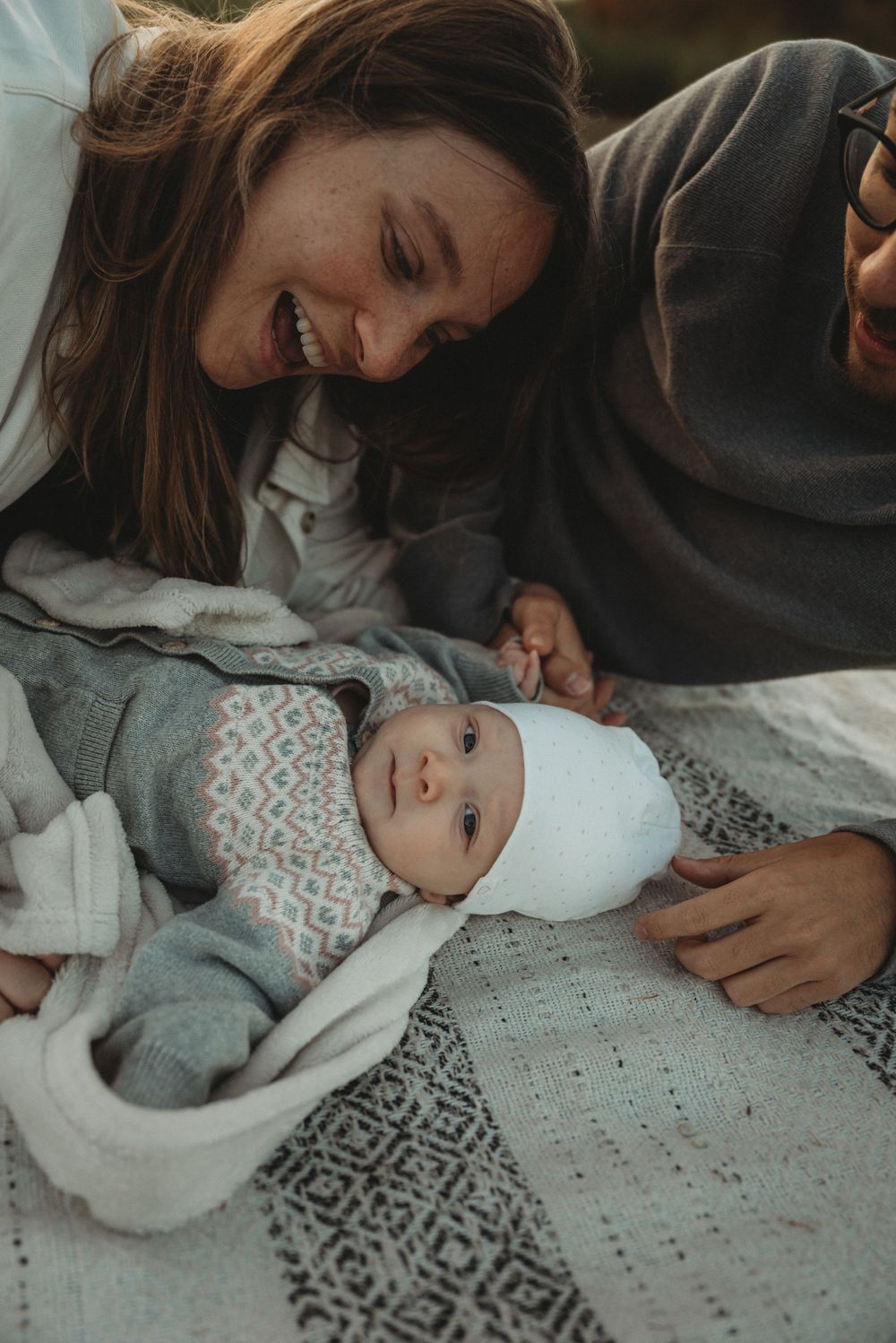 A tender family moment with parents gazing lovingly at their newborn baby wrapped in a patterned blanket.