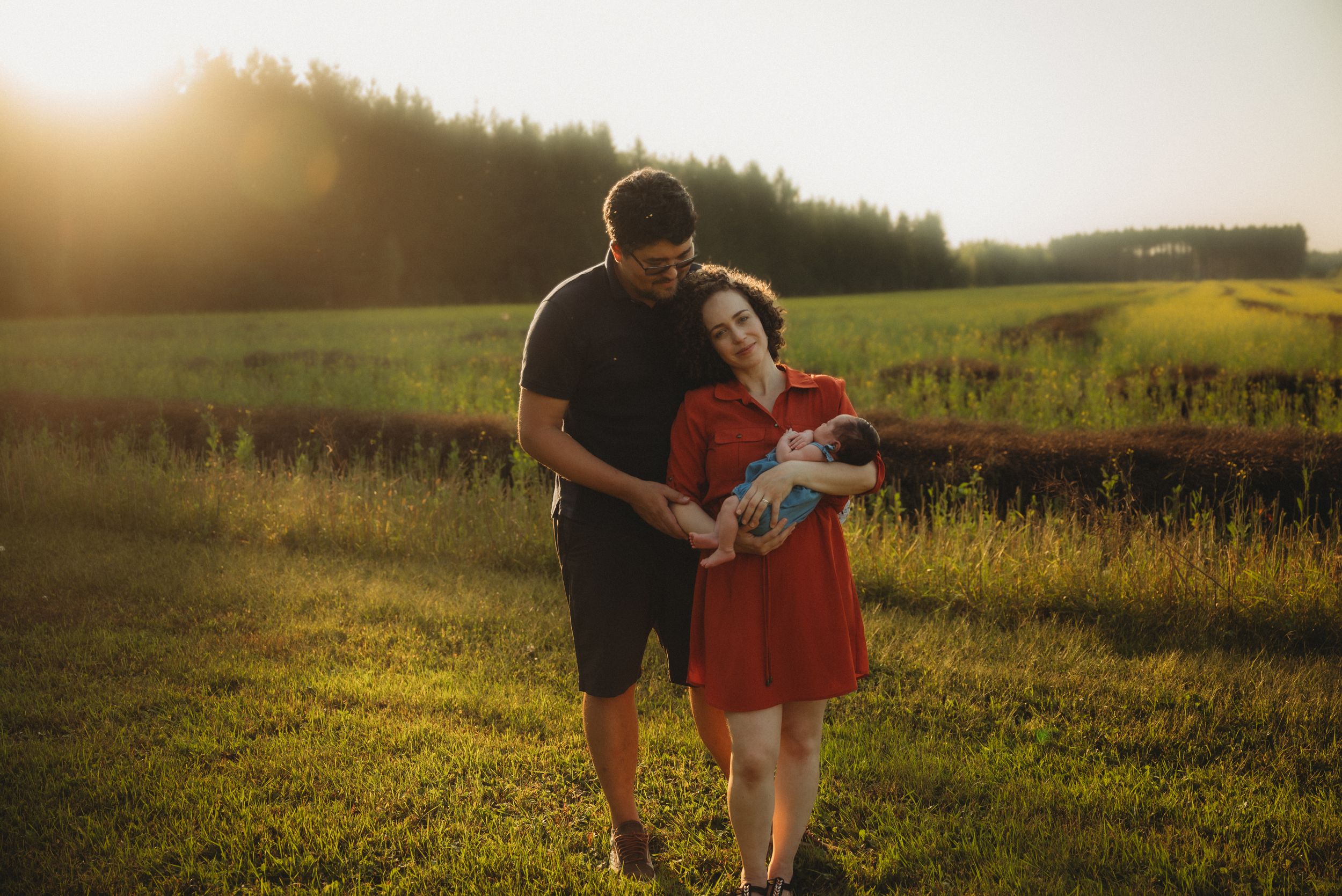 Couple shares an intimate moment with their baby in a sunlit meadow.