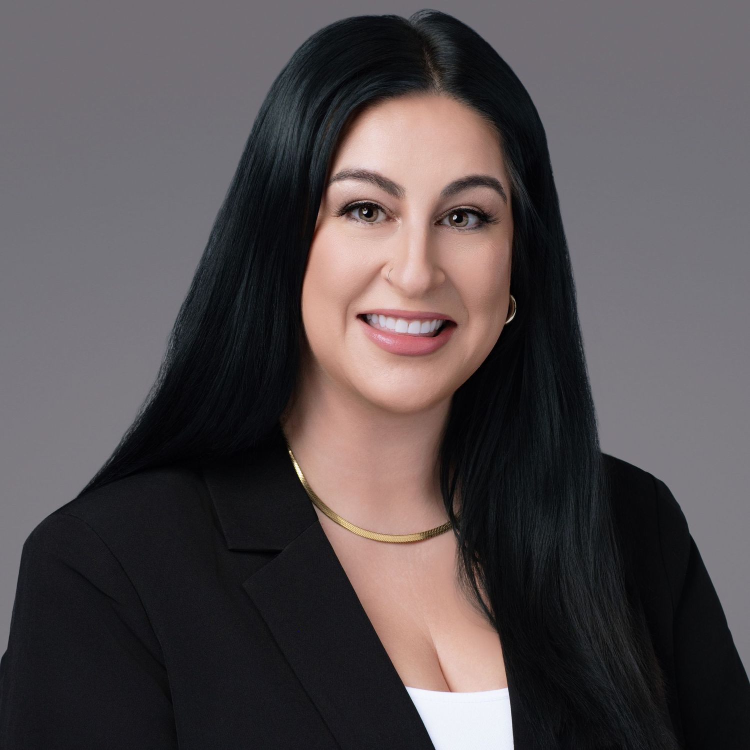 Professional business portrait of a woman in a black blazer with long dark hair and a delicate gold necklace.