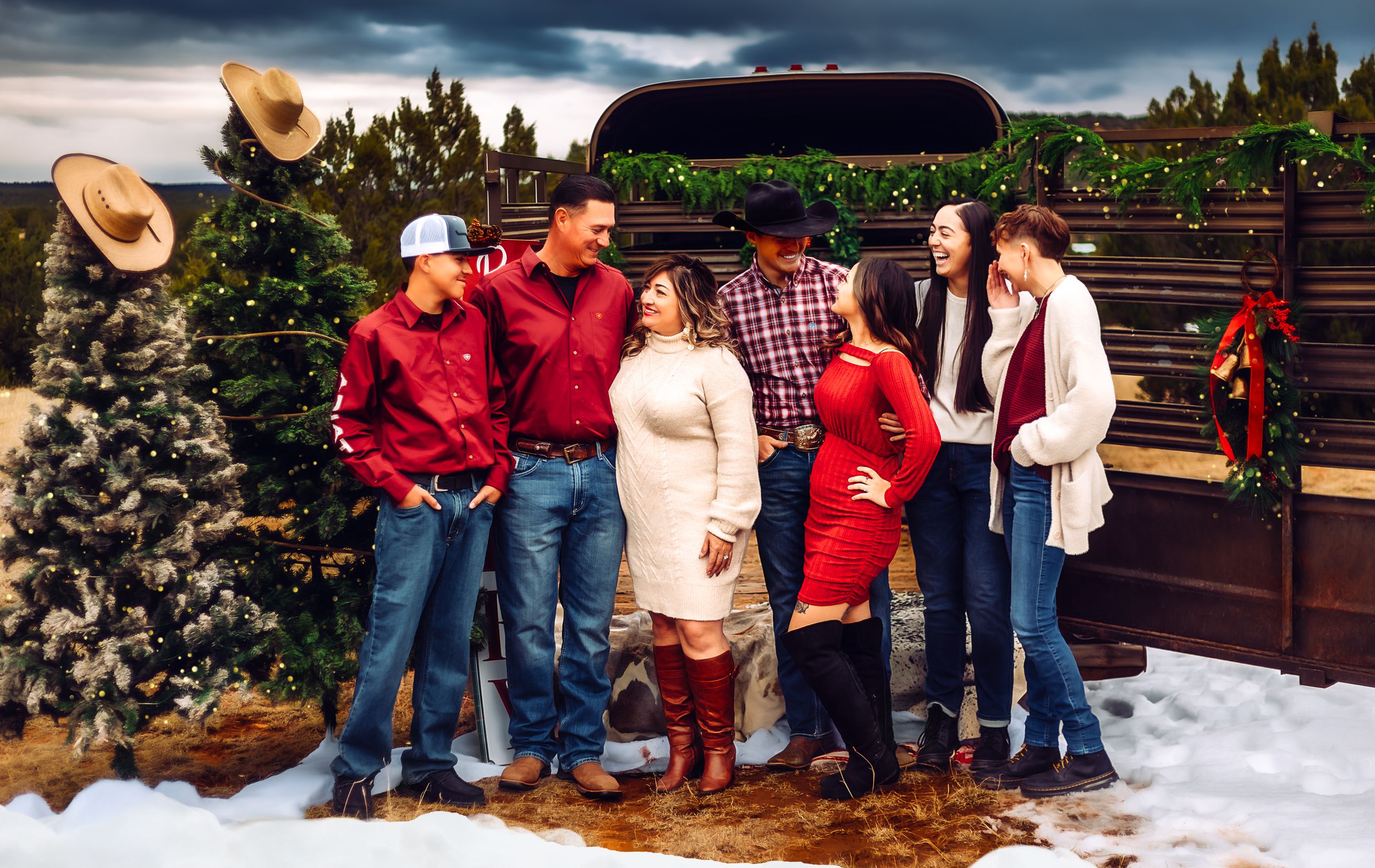 A festive group in red and casual attire poses outdoors in front of evergreen trees and snow during the holiday season.