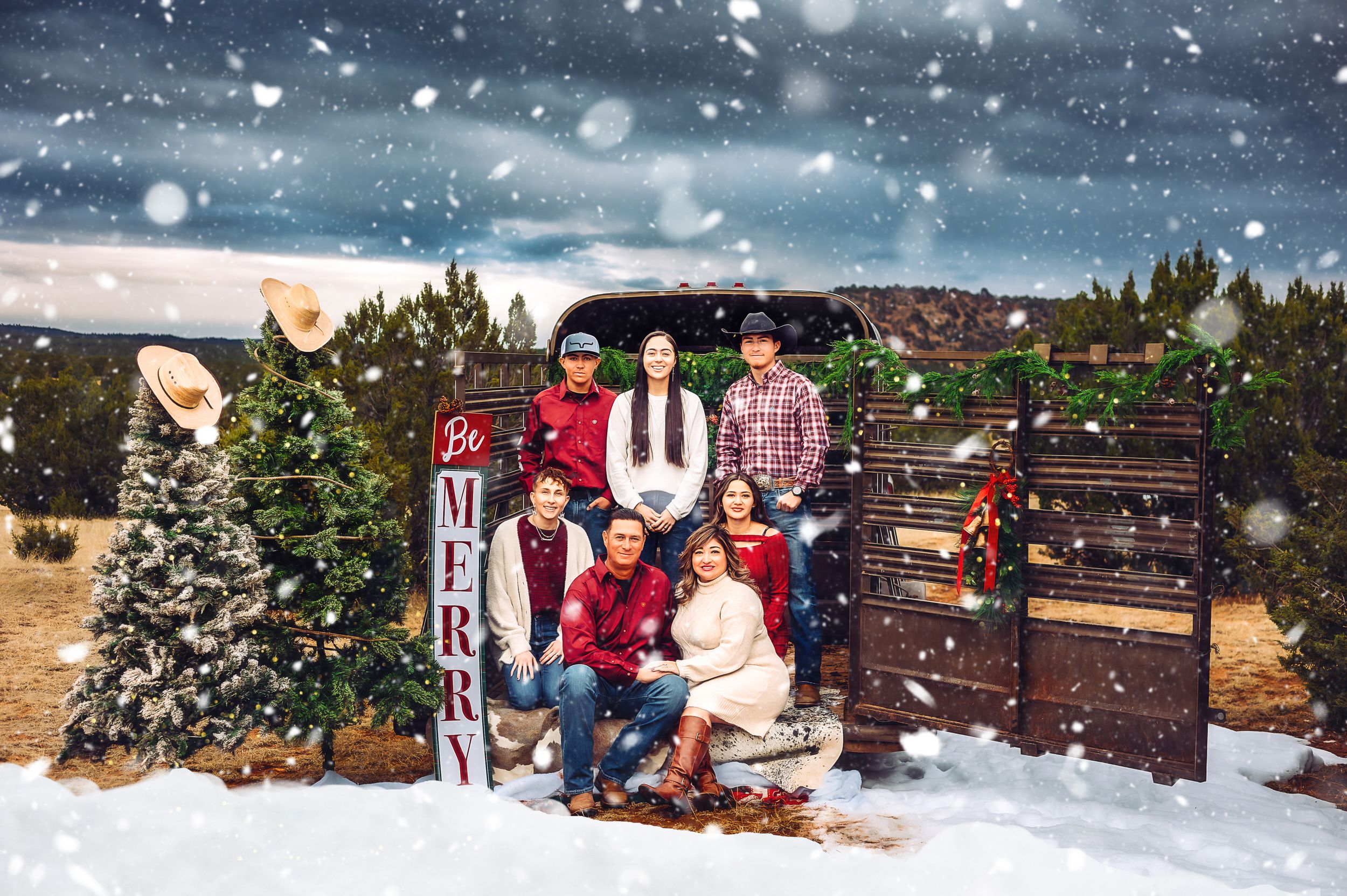 A family poses together on wooden stairs in a snowy outdoor setting with evergreen trees and falling snow.