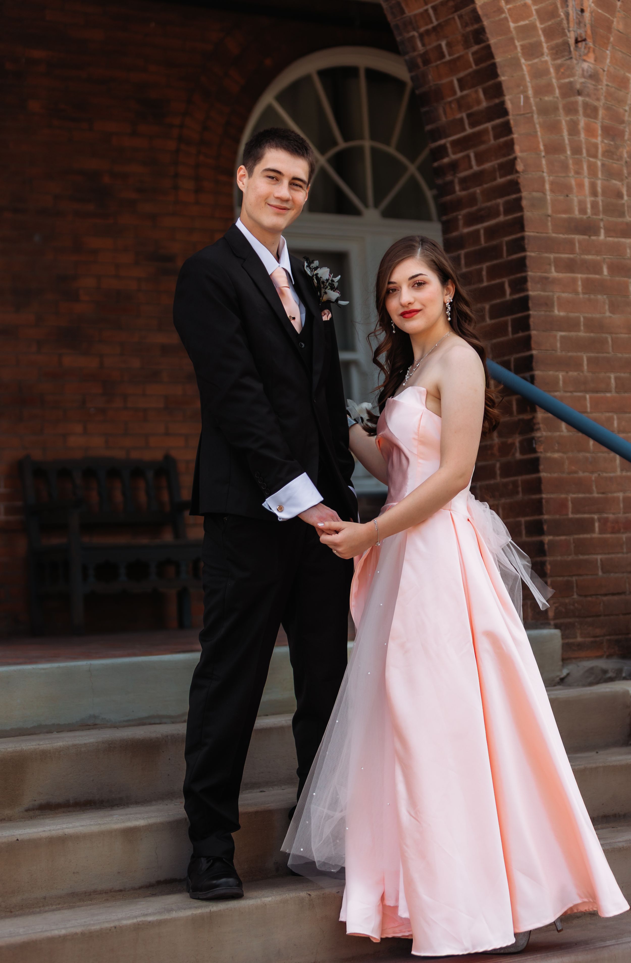 A couple in formal attire sharing a romantic dance moment against a brick wall background.