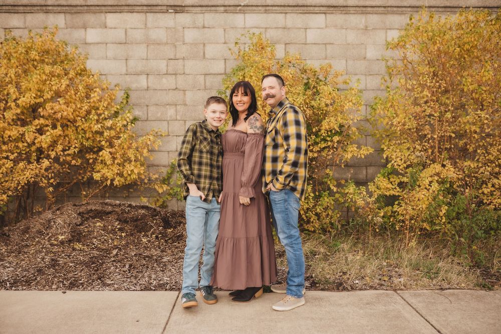 Three people stand together against a stone wall with golden yellow foliage in autumn.