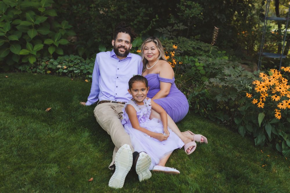 Three people sit together on grass with orange flowers blooming in a garden setting during summer.