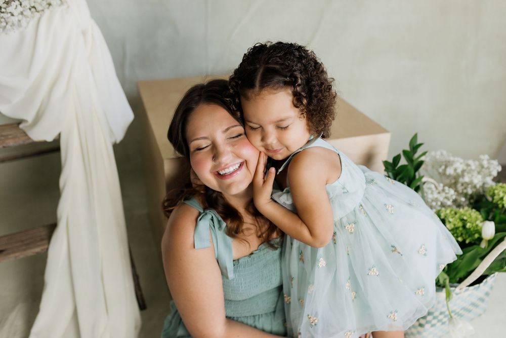 A parent and young child share a tender moment together while sitting indoors surrounded by flowers.