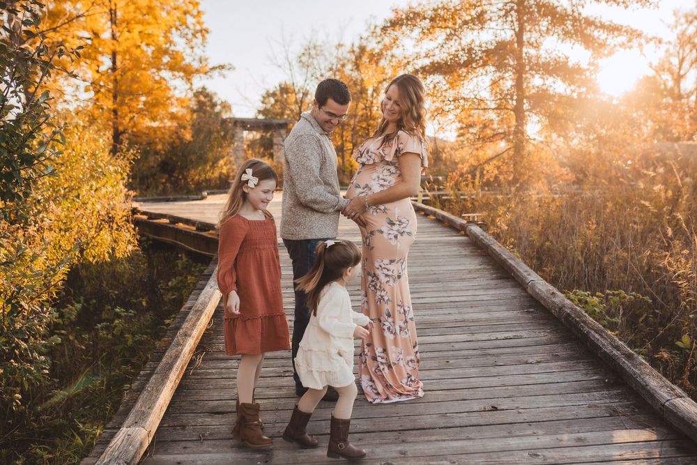 Family standing together on wooden bridge during golden sunset in autumn with orange foliage in background.