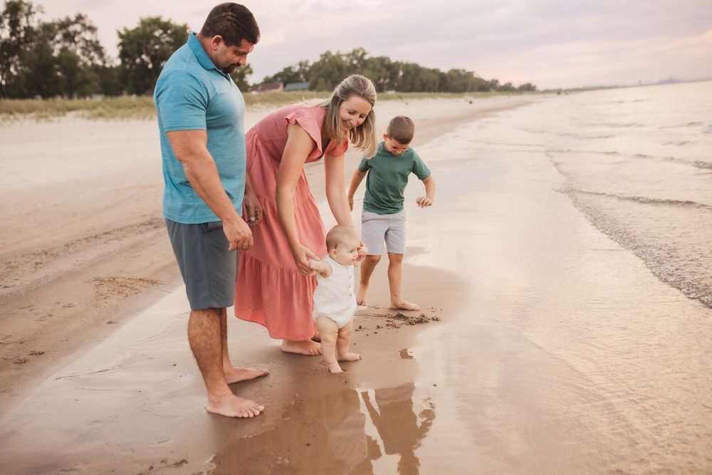 A family enjoys a peaceful evening walk along the shoreline at sunset, letting waves wash over their bare feet.