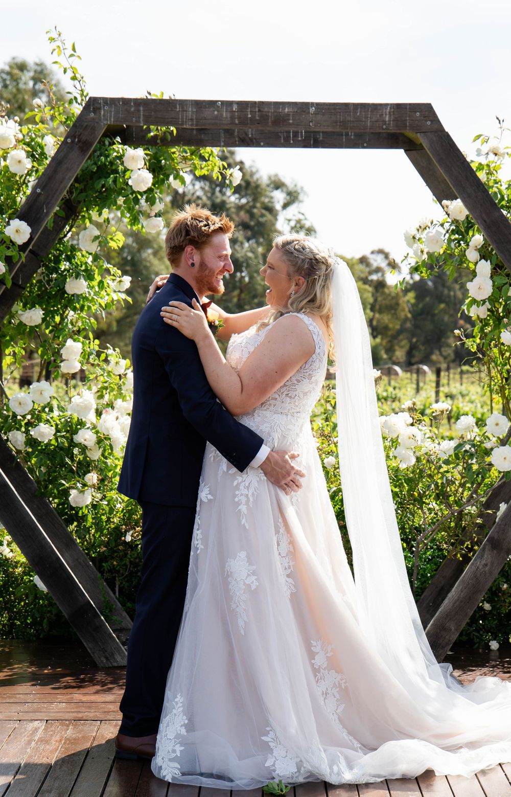 A couple embraces under a hexagonal wedding arch adorned with climbing greenery.
