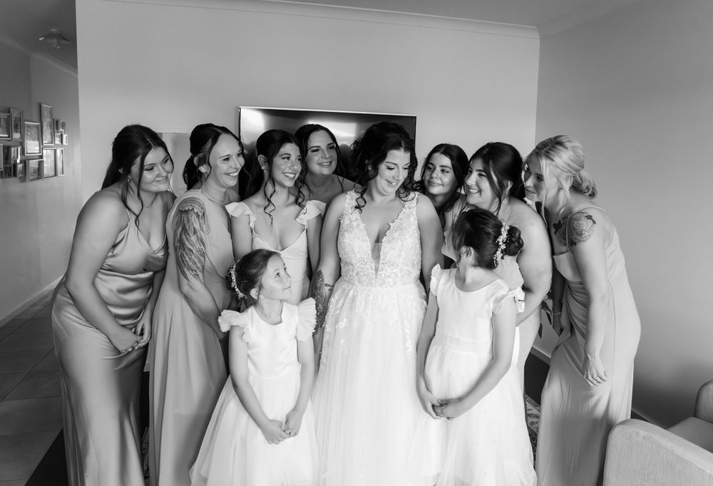Group in pale dresses gather together for a joyful bridal party photo.